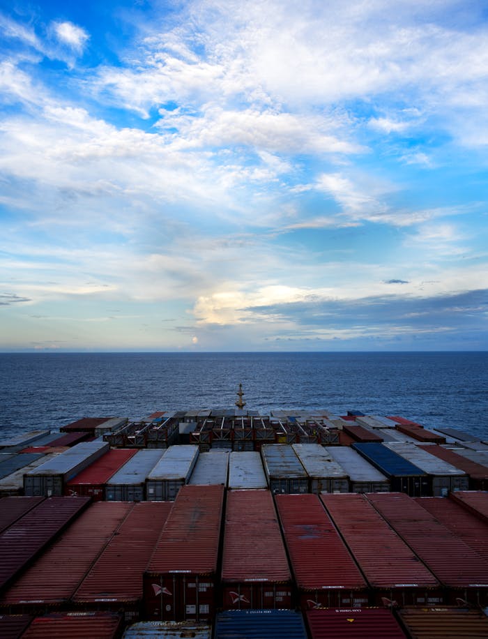 Aerial view of a cargo ship transporting containers over a calm ocean under a blue sky.